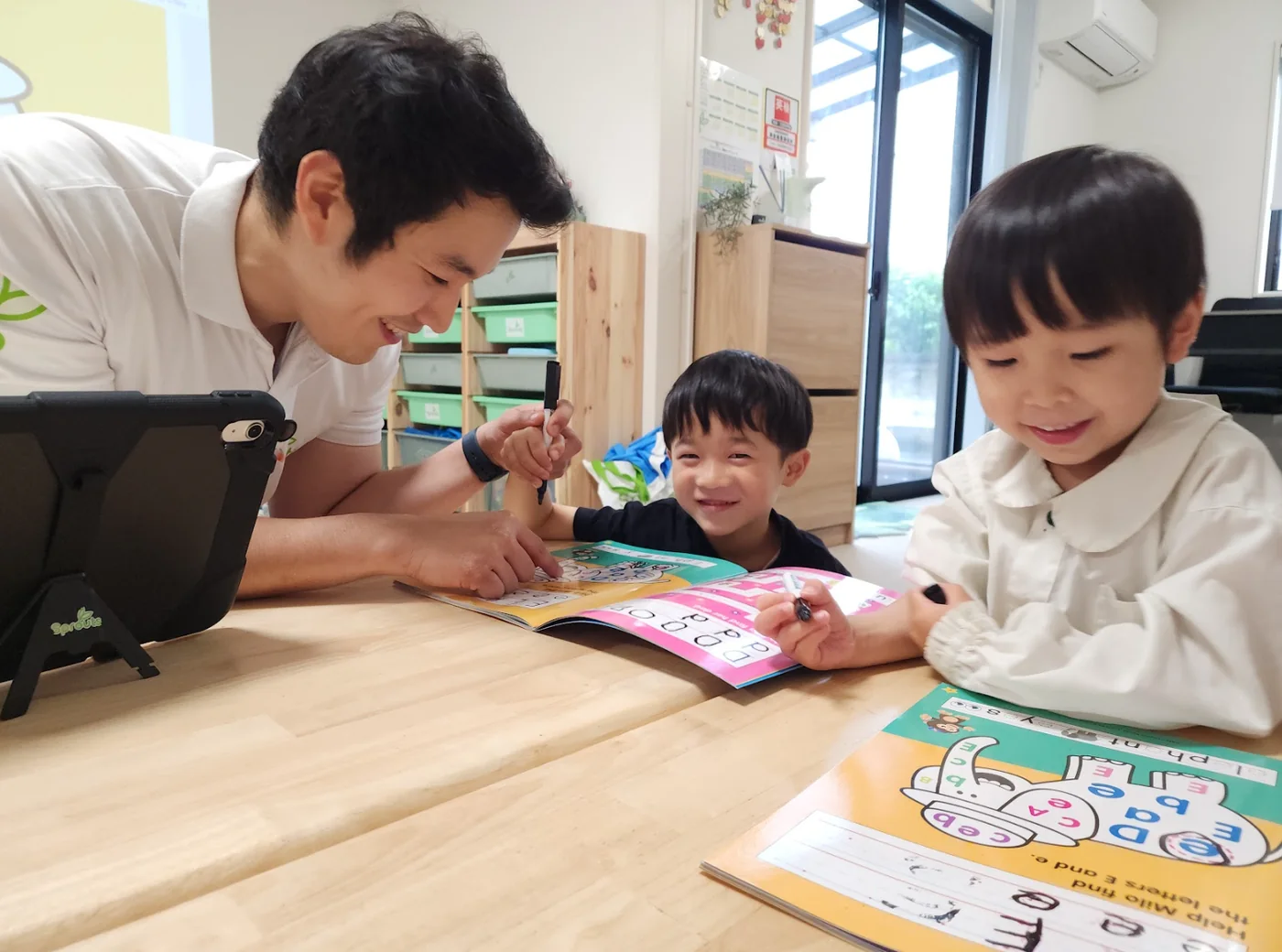 先生が幼児・低学年の子どもたちに英語のワークや文字への興味をサポートしている様子