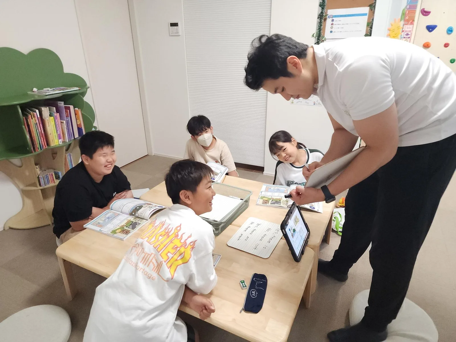 先生が子どもたちの様子を見ながらテーブルで英語を教えている様子
